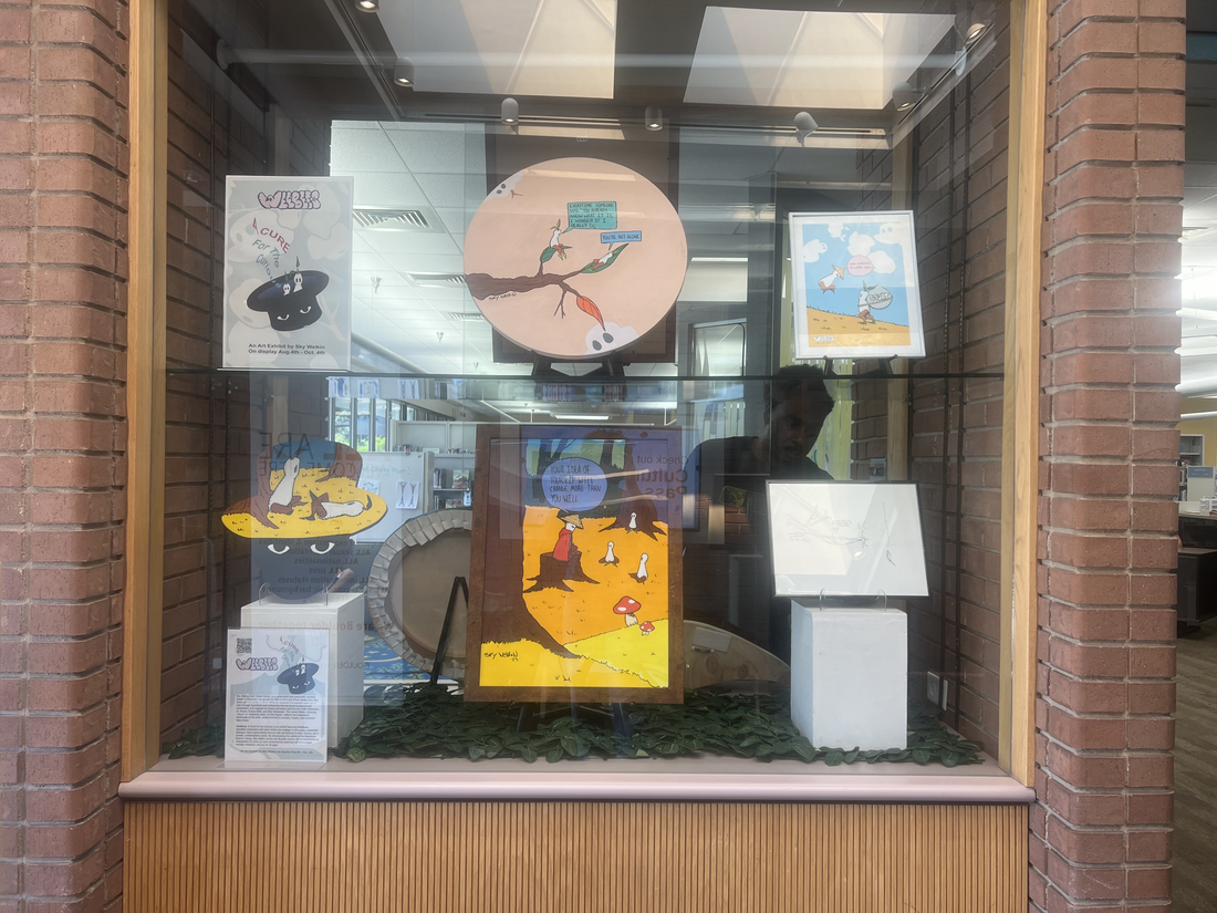 Library display case featuring artworks placed on two shelves.